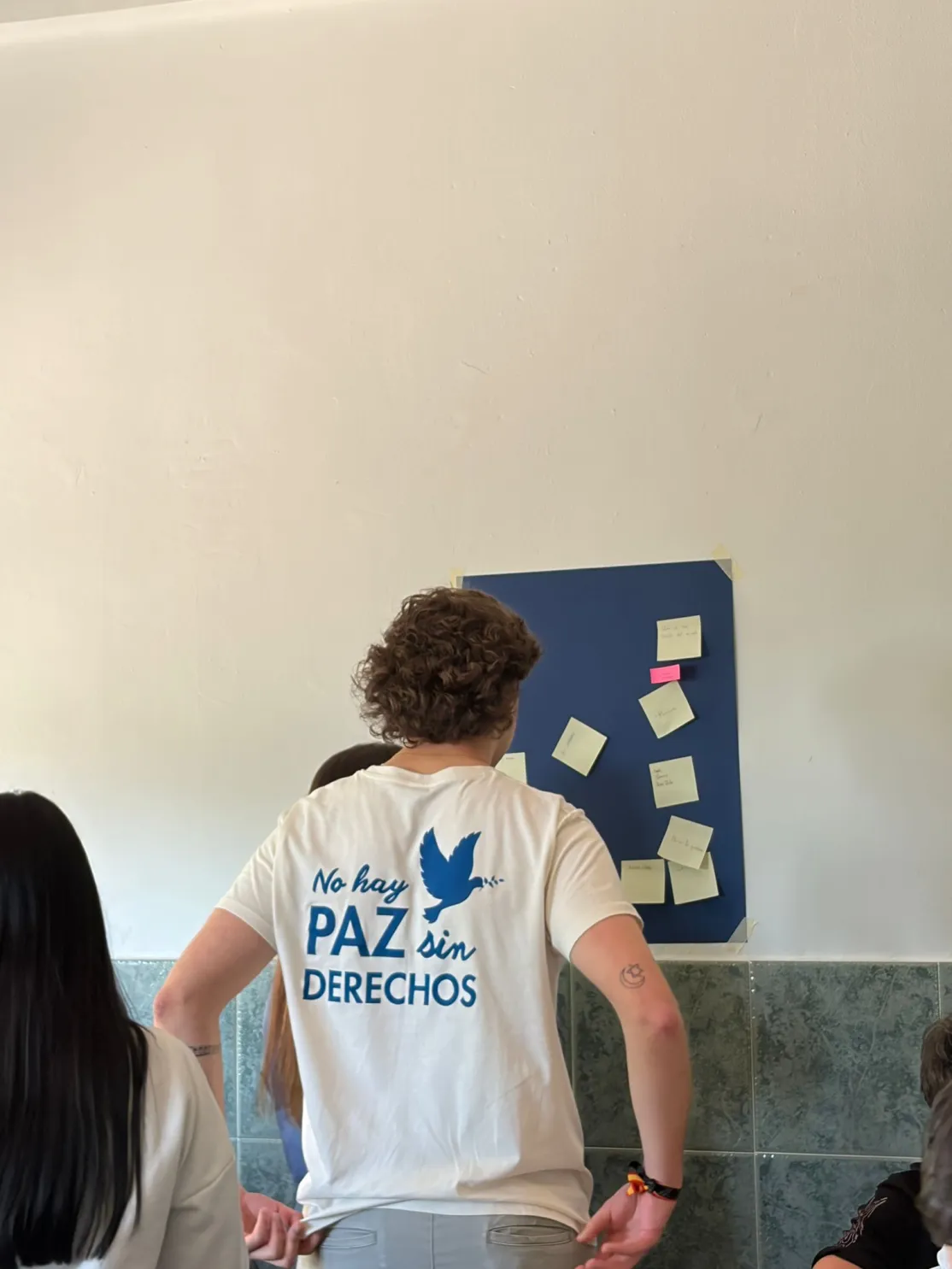 Un joven voluntario observa un mural con notas adhesivas durante una dinámica de reflexión en el aula.