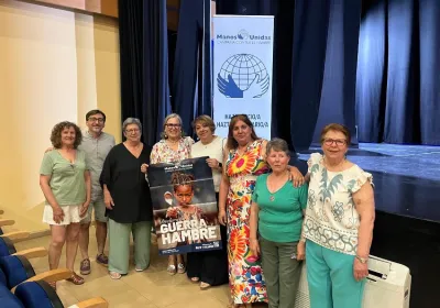 Representantes y personas voluntarias posan en el Auditorio de Montehermoso junto a un cartel de la campaña «Declara la guerra al hambre» y un expositor de Manos Unidas.