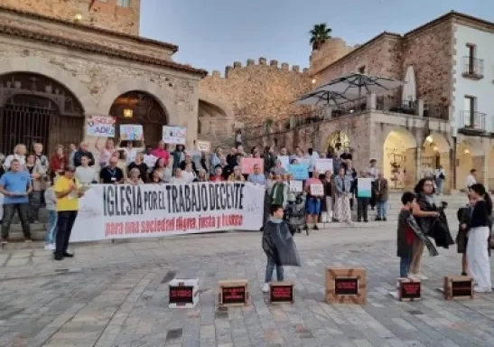 Numerosas personas participan en la concentración por el trabajo decente frente a la Ermita de la Paz, sosteniendo pancartas y una gran lona con el mensaje «Iglesia por el trabajo decente».
