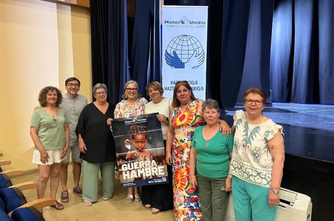 Representantes y personas voluntarias posan en el Auditorio de Montehermoso junto a un cartel de la campaña «Declara la guerra al hambre» y un expositor de Manos Unidas.