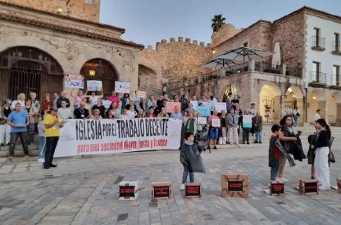 Numerosas personas participan en la concentración por el trabajo decente frente a la Ermita de la Paz, sosteniendo pancartas y una gran lona con el mensaje «Iglesia por el trabajo decente».