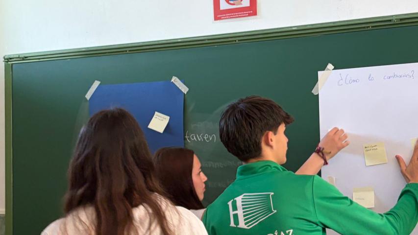 Tres estudiantes colocan notas adhesivas en un mural durante una actividad participativa realizada en el aula.