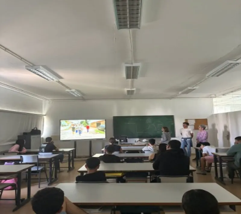 Alumnado sentado en un aula durante una sesión de sensibilización impartida por Manos Unidas, con una presentación audiovisual al frente.