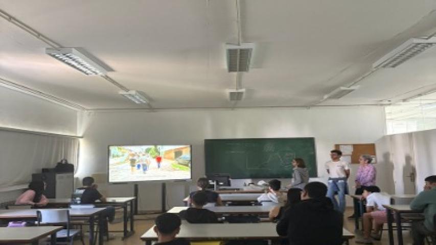 Alumnado sentado en un aula durante una sesión de sensibilización impartida por Manos Unidas, con una presentación audiovisual al frente.