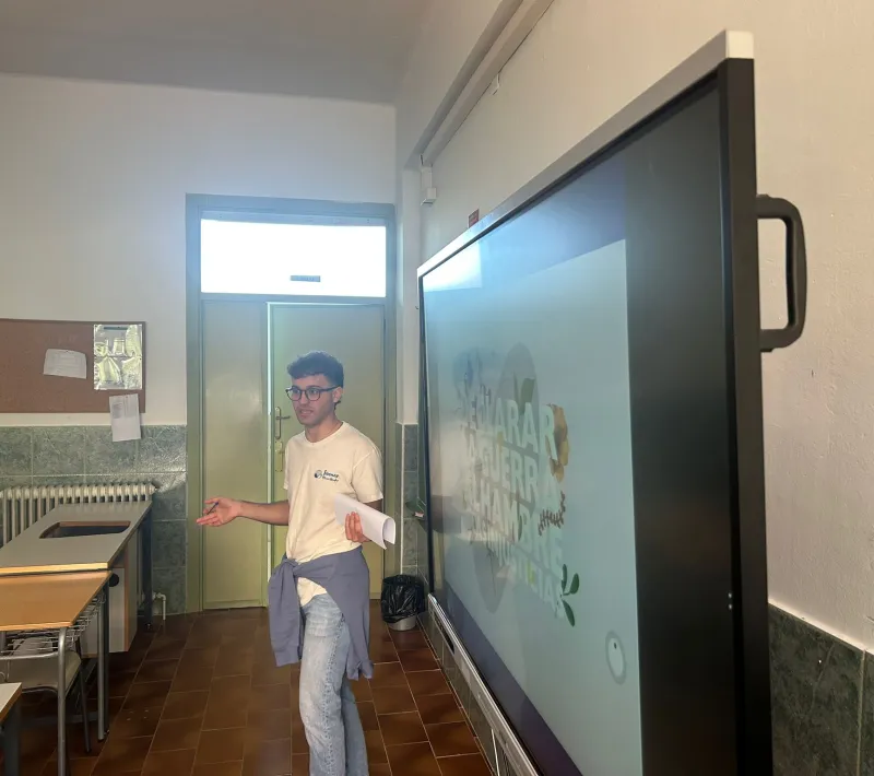 Un joven voluntario de Manos Unidas realiza una presentación en el aula junto a una pantalla digital.