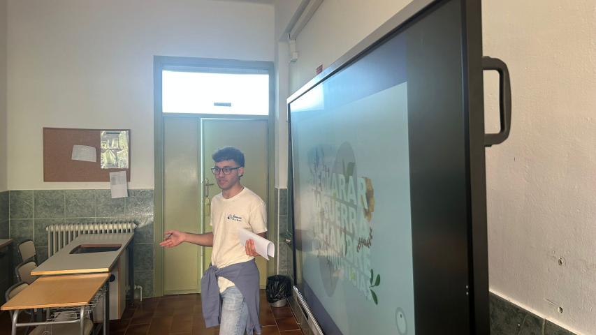 Un joven voluntario de Manos Unidas realiza una presentación en el aula junto a una pantalla digital.