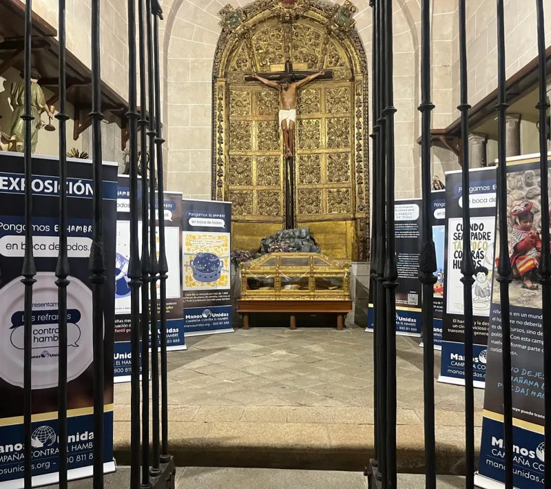 Paneles de la exposición instalados en una capilla, a ambos lados de un retablo dorado con un crucifijo, vistos a través de una reja.