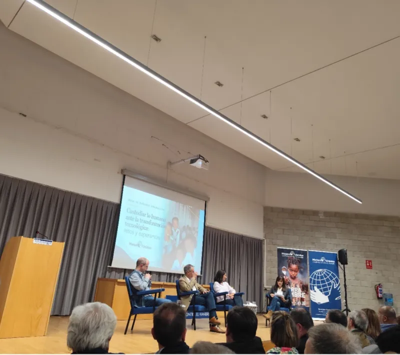 Vista del auditorio durante la mesa de diálogo «Custodiar lo humano ante la transformación tecnológica: retos y esperanzas», con cuatro participantes en el escenario y el público en primer plano.