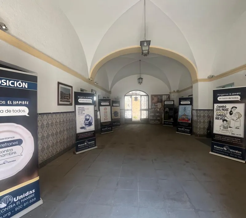 Paneles de la exposición «Los refranes de Manos Unidas» distribuidos a ambos lados de un amplio pasillo abovedado en la Oficina de Turismo de Montehermoso.