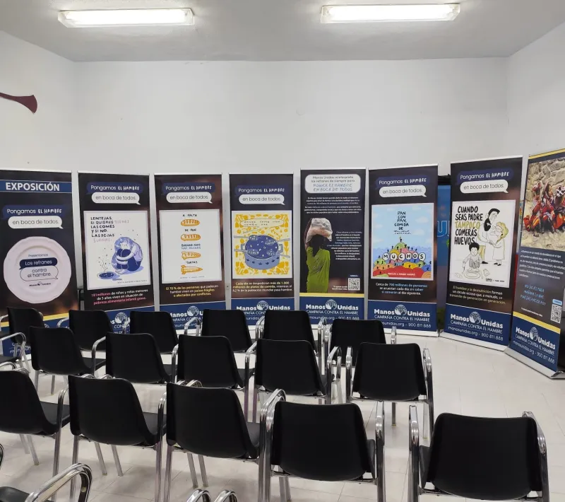 Paneles de la exposición alineados detrás de varias filas de sillas negras en una sala preparada para recibir a los visitantes.