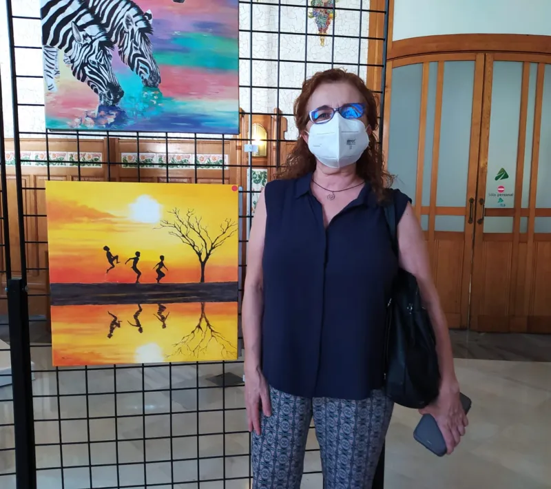 La autora posa junto a su cuadro en la exposición a beneficio de Manos Unidas Valencia.