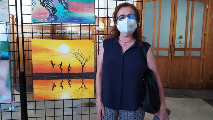 La autora posa junto a su cuadro en la exposición a beneficio de Manos Unidas Valencia.